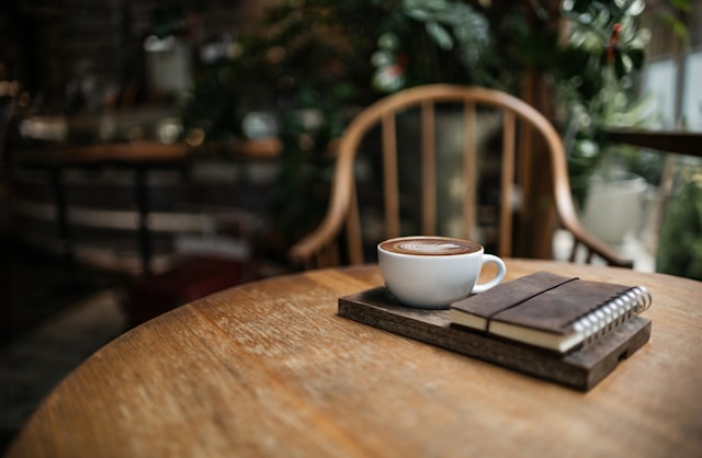 木のテーブルに置かれたコーヒーと手帳